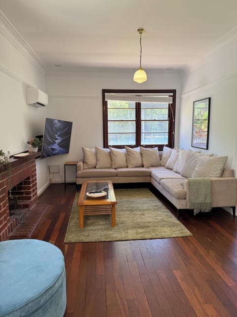 A cozy living room features a spacious sectional sofa with plush cushions, a smart TV for entertainment, efficient air conditioning, and a charming fireplace for added ambiance.