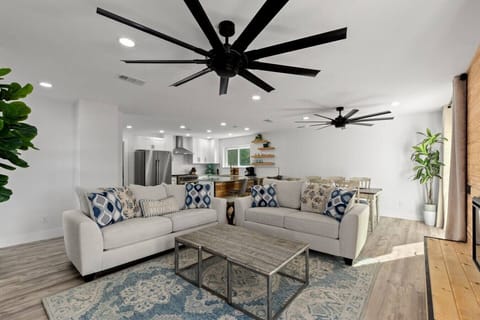 A bright, open living room with a fireplace and natural light effortlessly connects to the kitchen and dining area, with three easy access points to outdoor spaces for seamless indoor-outdoor living.