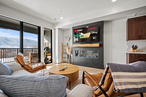 Experience the cozy living room, outfitted with plush seating, a fireplace, an expansive smart TV, and patio doors that frame the breathtaking mountain vistas.