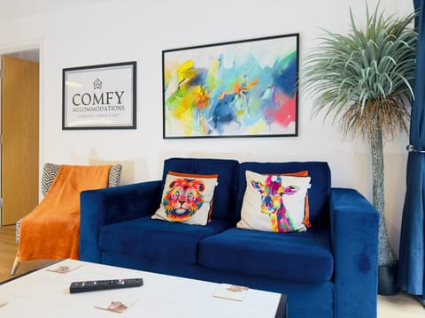 Bright and stylish living room with floor-to-ceiling windows, flooding the space with natural light. Features a plush blue sofa, a modern coffee table, and a smart TV for your entertainment. Perfect for relaxing after a day exploring the city. Seamlessly connects to the bedroom for a cozy, open-plan feel.