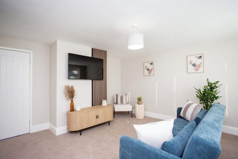 Modern living room with a cozy blue sofa, wall-mounted TV, and stylish decor. Bright, inviting, and comfortable.