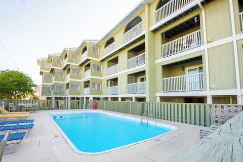 Multi-story vacation rental building with balconies overlooking a central swimming pool area with poolside seating and lounge chairs.