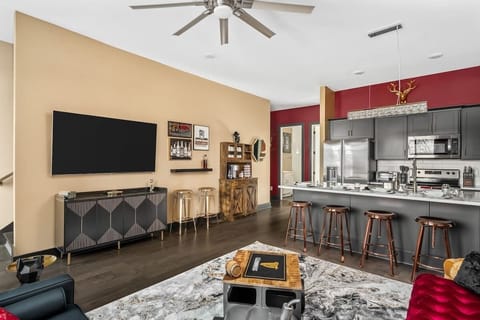 Unwind in this stylish open-concept living space featuring a sleek kitchen, bold decor, and a cozy lounge with a large smart TV. Perfect for entertaining or relaxing in a chic, modern atmosphere with vibrant touches and bar-style seating.
