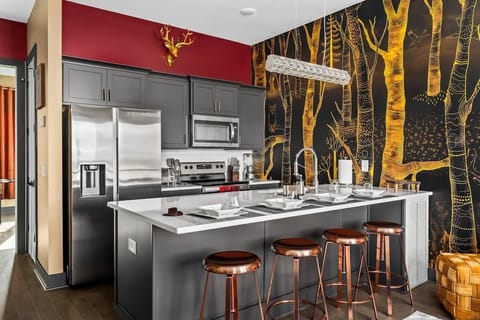 Stylish kitchen with modern appliances, sleek gray cabinetry, and a whimsical forest mural. Gather around the chic island with copper stools for meals, drinks, or conversation in this bold and artsy space.
