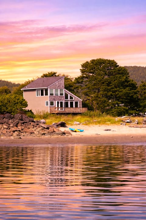 Waterfront property with private beach access beneath a stunning pastel sunset sky, surrounded by natural forest landscape.