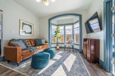 - Bright living room with bay windows filling the space with natural light   - Modern leather sofa and plush ottomans for relaxing evenings   - Smart TV setup perfect for streaming and cozy gatherings