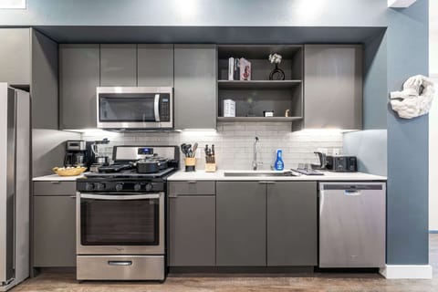 A fully equipped designer kitchen with sleek gray cabinetry, marble backsplash, and stainless-steel appliances — crafted for modern living.