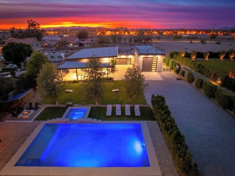 Modern vacation rental featuring dual swimming pools and hot tub, set against a stunning desert sunset backdrop with spacious outdoor entertaining areas and landscaped grounds.