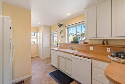 A luxury kitchen and prep area, featuring bright white cabinetry, a deep sink with a window view, and a built-in dishwasher, perfect for efficient meal cleanup or staying organized while cooking.