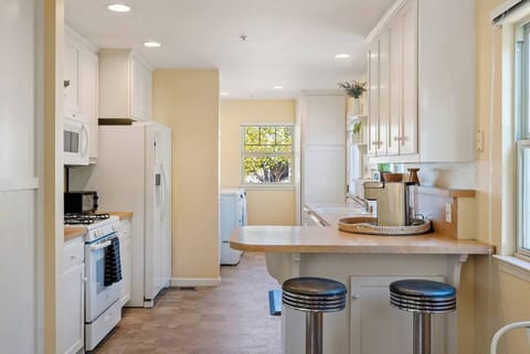A streamlined kitchen and breakfast bar, featuring dual retro-style chrome stools, integrated prep space, and a bright view into the laundry area, perfect for quick morning bites or casual conversation while cooking.
