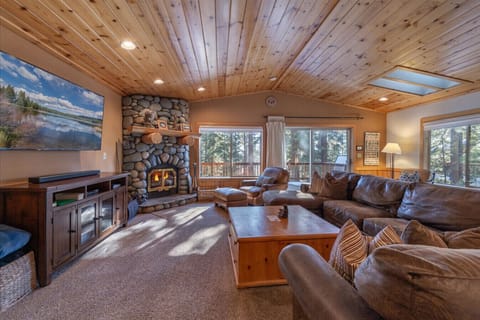 Large open great room (living room, dining area, kitchen) with river rock fireplace, beautiful furnishings, and 60 inch SmartTV.