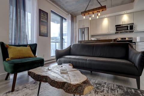 A stylish and inviting living space with a modern black leather sofa, warm lighting, and an open flow into the kitchen.
