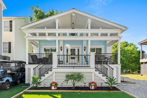 Front porch with light blue shingle siding, white columns, black metal railing, and outdoor seating areas.