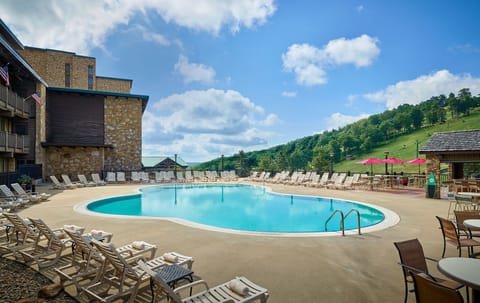 Sparkling pool with clear blue skies and lush green hills as the backdrop, offering a serene outdoor retreat.