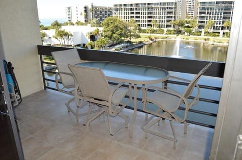 Living room opens to a balcony with beige tile flooring and glass-top table seating three overlooking a fountain pond.
