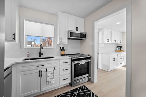 Contemporary chalet kitchen featuring tailor-made quartz countertops and brand-new appliances, effortlessly flowing into a sunlit laundry area and coffee bar. This space opens up to the backyard patio, providing plentiful cabinetry and an airy layout