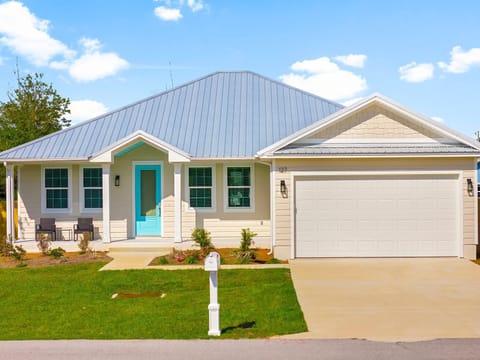 Modern coastal-style home with charming turquoise door and metal roof in peaceful residential neighborhood.