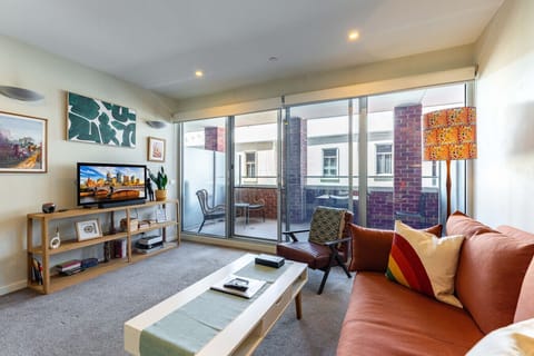 A cozy living room with a TV, comfy furniture, and a sunny balcony