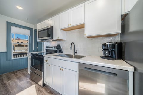 Compact yet efficient kitchen with modern amenities like a microwave, oven, dishwasher, and coffee maker. The island provides additional counter space and seating. White cabinetry and subway tile backsplash for a clean look.