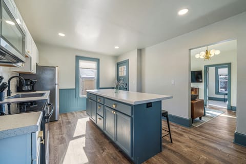 Bright and airy kitchen with modern appliances, including a microwave, coffee maker, and fridge. Features a spacious island with seating, perfect for casual dining or socializing. Opens to a cozy living area with warm lighting.