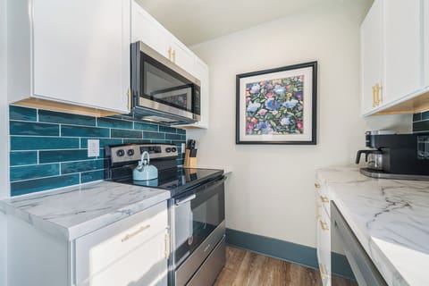 Enjoy this compact yet efficient kitchen with ample storage in white cabinets accented by gold handles. A built-in microwave and oven make cooking convenient, while a blue tile backsplash adds a splash of color.