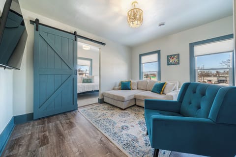 Unwind in this inviting living room with plush seating options, including a sectional sofa with colorful accents and a chic armchair. The room is enhanced by artistic decor, a vintage radio cabinet. Offering a blend of vintage and contemporary charm.