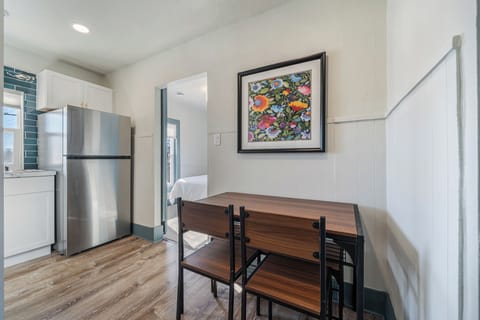 Step into this compact yet functional kitchen with sleek stainless steel appliances, including a large refrigerator. The space is adorned with stylish art and features a practical dining table with seating for four.