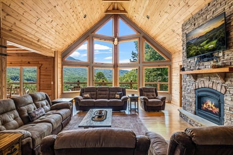 Cozy up by the stone fireplace in this stunning living room, featuring soaring ceilings, a wall of windows, and breathtaking Smoky Mountain scenery.
