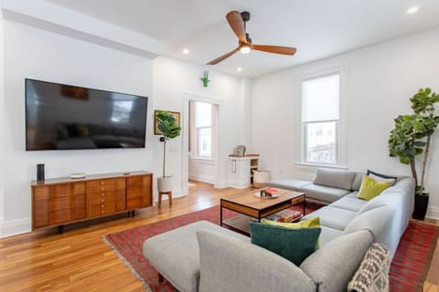 A spacious living area featuring a wall-mounted flat screen TV, complemented by a large window that lets in plenty of natural light, creating a bright and airy atmosphere.
