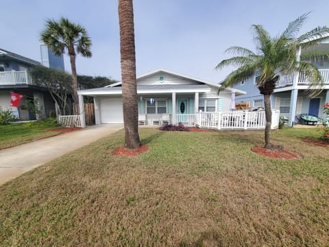 Charming beach house with a welcoming front porch and lush palm trees.
