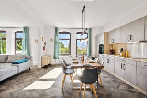 Offene Wohnküche mit modernem Esstisch, stilvoller Beleuchtung und großen Fenstern, die viel Tageslicht hereinlassen.