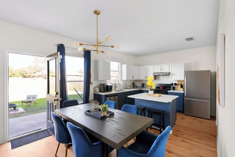 Modern dining area with a stylish wood table, plush blue chairs, and a chic open kitchen. Perfect for family meals after a day at Dell Diamond or Kalahari! The open layout leads to a private backyard, great for relaxing or enjoying the Texas sunshine