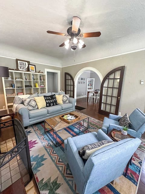 Relax in this spacious living room featuring light blue armchairs, a matching sofa, a patterned rug, a wooden coffee table, and an arched doorway leading to an adjoining room.