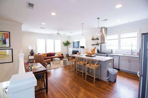 Cook, dine, and relax in this open-concept living space featuring a modern kitchen with a large island and bar seating, flowing seamlessly into a cozy living area with a sofa, fireplace, and hardwood flooring throughout.
