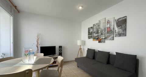 Bright and modern living-dining room with a comfortable sofa, TV, and table. Large windows provide natural light, creating a cozy atmosphere perfect for relaxing after exploring the area.