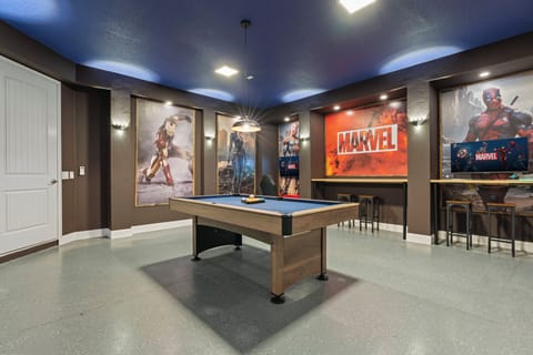 Dive into fun in this vibrant game room, featuring a sleek pool table at its center, surrounded by striking Marvel-themed artwork. The bold blue ceiling lights the space, creating a lively atmosphere for friendly competition.