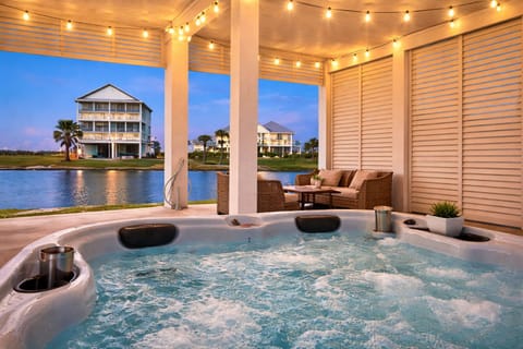 Covered outdoor living space with hot tub, string lighting, and lounge seating—ideal for relaxing evenings at this Galveston coastal getaway.