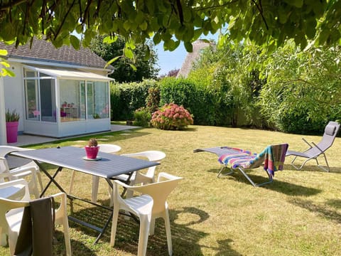 A large, sunny garden with a table, chairs, lounge chairs, and a veranda at Maison Karome in Saint-Coulomb.