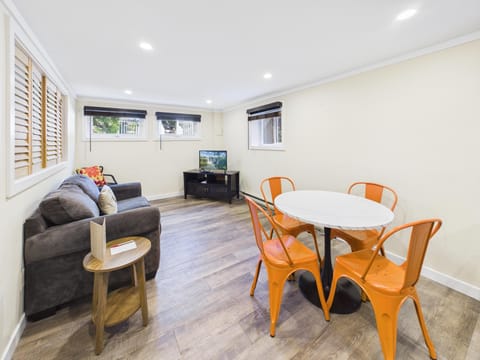 Living area with gray sofa, round white dining table, four orange metal chairs, and wood-look vinyl flooring.