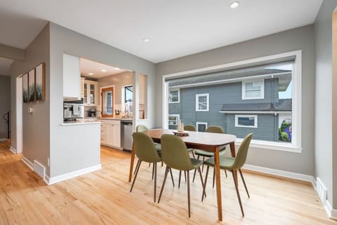 MAIN FLOOR-DINNING ROOM: A sleek wooden table with six olive-green chairs sits by a large window, filling the space with natural light. The open layout connects seamlessly to the kitchen with the dining room.