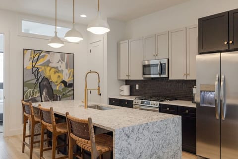 A contemporary kitchen with stainless steel appliances, a large marble island, and elegant pendant lighting.