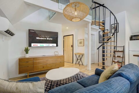 Welcome to Modern Slate! Stylish loft-style living area with a plush sectional, Smart TV, and a striking spiral staircase leading to the upper level.
