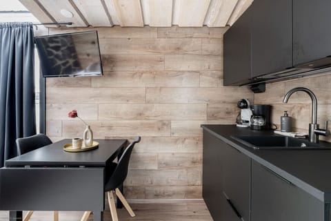 Enjoy a meal or a cup of coffee at the stylish dining table, which is also a perfect spot for remote work. The sleek, black furniture beautifully contrasts with the warm wood-paneled wall, while a well-placed wall-mounted TV provides entertainment.