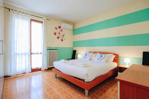 Spacious and colorful double bedroom in an apartment in Peschiera del Garda, tastefully furnished with lively details. The large windows with light curtains provide natural light and direct access to the balcony. Perfect for those looking for a relaxing and informal environment, just a few minutes from the beaches and the historic center.