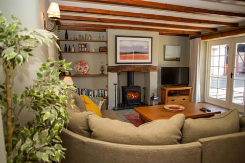 Living room with shelving, wood burner, large corner sofa, TV, coffee table and French doors leading to the patio