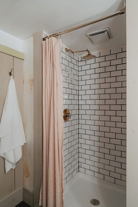 The Fitzgerald Room’s private detached bathroom offers a refreshing subway-tiled shower, warm brass finishes, and vintage-inspired details for a luxurious experience.