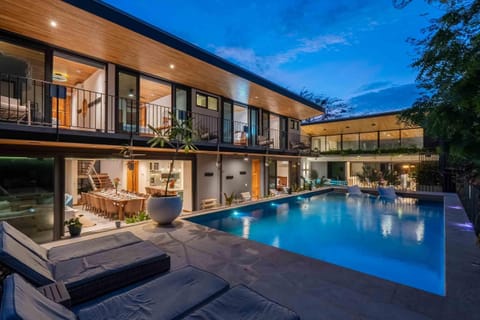 Outdoor pool area with cushioned loungers, stone decking, and a two-story balcony.