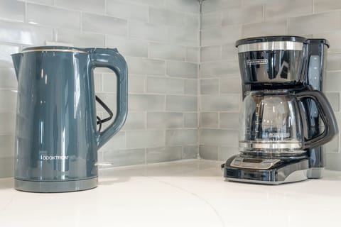 Coffee corner with kettle, drip maker, and glossy subway tile backsplash.