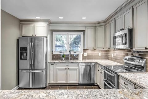 - Well appointed kitchen includes French door fridge, dishwasher, and window view
- Gorgeous granite counters and gray cabinets elevate the space with elegance
- Fully stocked for cooking, coffee, or entertaining with ease and charm