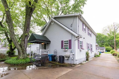 Light gray vacation rental with purple shutters and welcoming entrance canopy, nestled in a lush, tree-lined neighborhood with convenient driveway parking.
